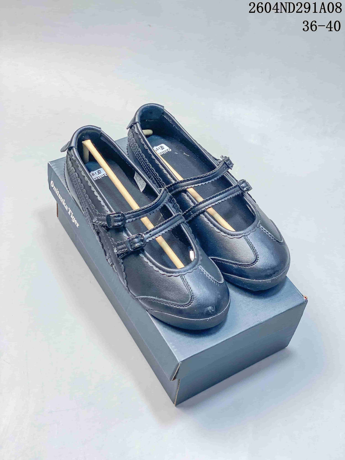 Pair of black Onitsuka Tiger Mary Jane-style sneakers displayed on a shoebox, with two buckle straps and a visible 36–40 size range.
