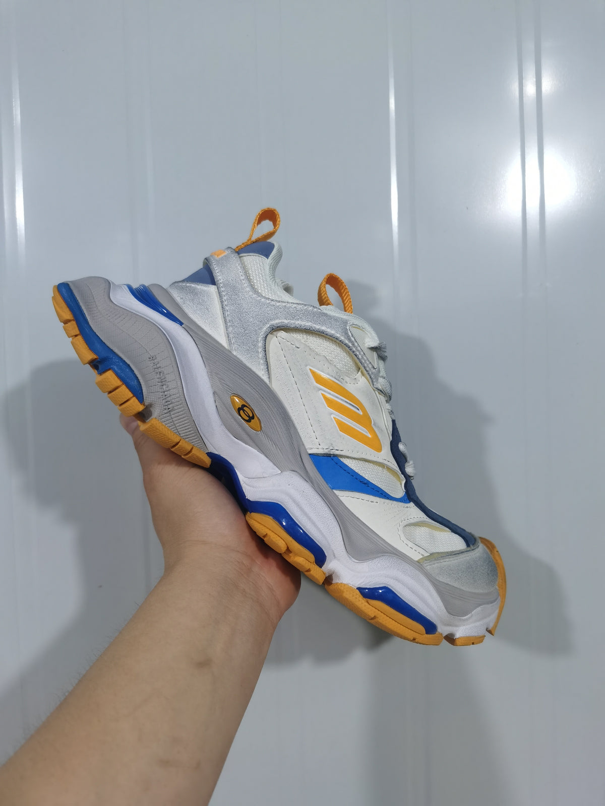 New Balance 9174 sneaker shown at an angle, highlighting the layered white and grey upper with orange and blue accents.