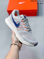 Angled side view showing the gray upper, navy Nike Swoosh, orange accents and raised white midsole.