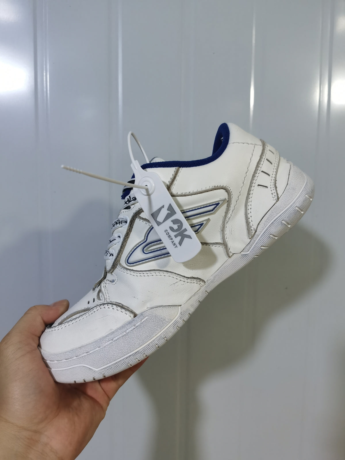Angled view of the white and blue Balenciaga Hampton sneaker showing the heel construction, side emblem, and attached hangtag.