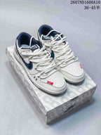 Pair of white and navy Nike SB Dunk Low sneakers displayed on a patterned shoe box, with style code and size range text visible above.