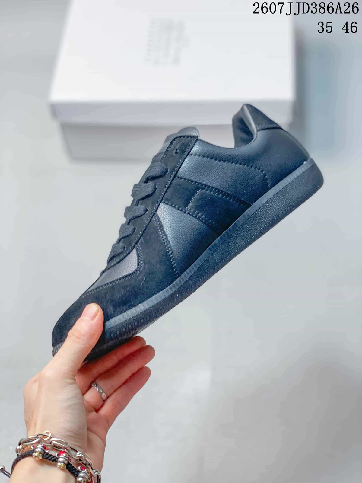 Side view of the black sneaker showing layered stitched panels, tonal upper sections, laces, and a low rubber sole.