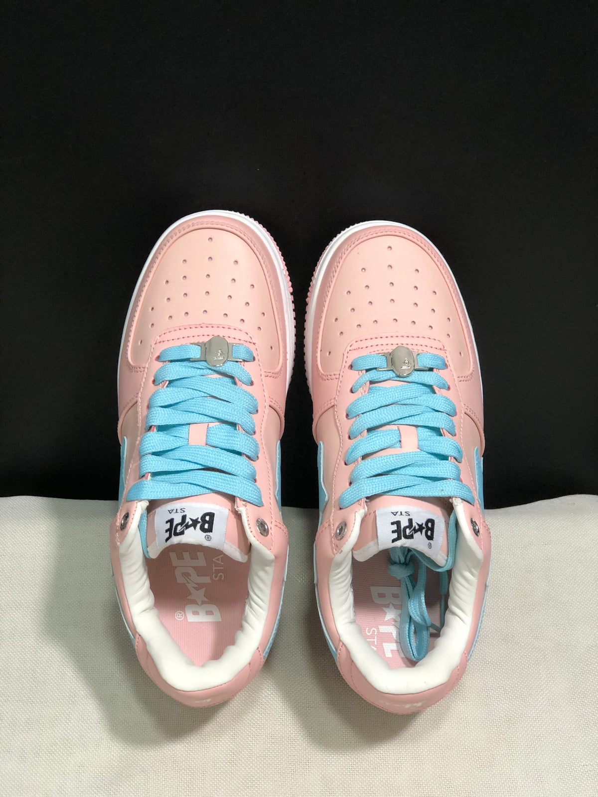 Top-down view showing the perforated pink toe boxes, light-blue laces, metal lace details, and branded tongues.