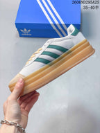Side profile of the white Adidas sneaker with green stripes and a thick layered gum-colored sole.