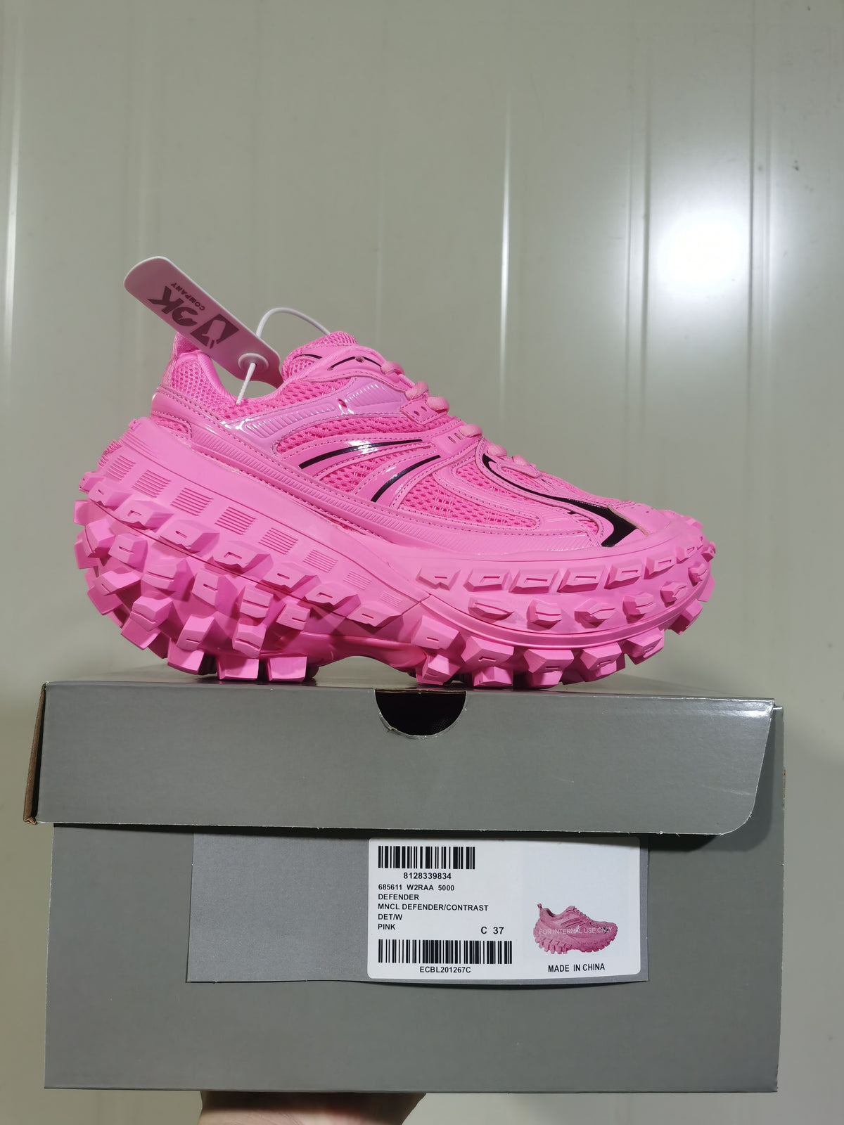 Bright pink chunky sneaker displayed on its box, showing the layered upper, black accents, lugged outsole, and box label.