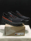 Pair of black and orange On Cloudmonster 1 sneakers displayed on a branded shoe box; the box label shows a photographed size of US 8, EU 41, UK 7.5, and JP 26.