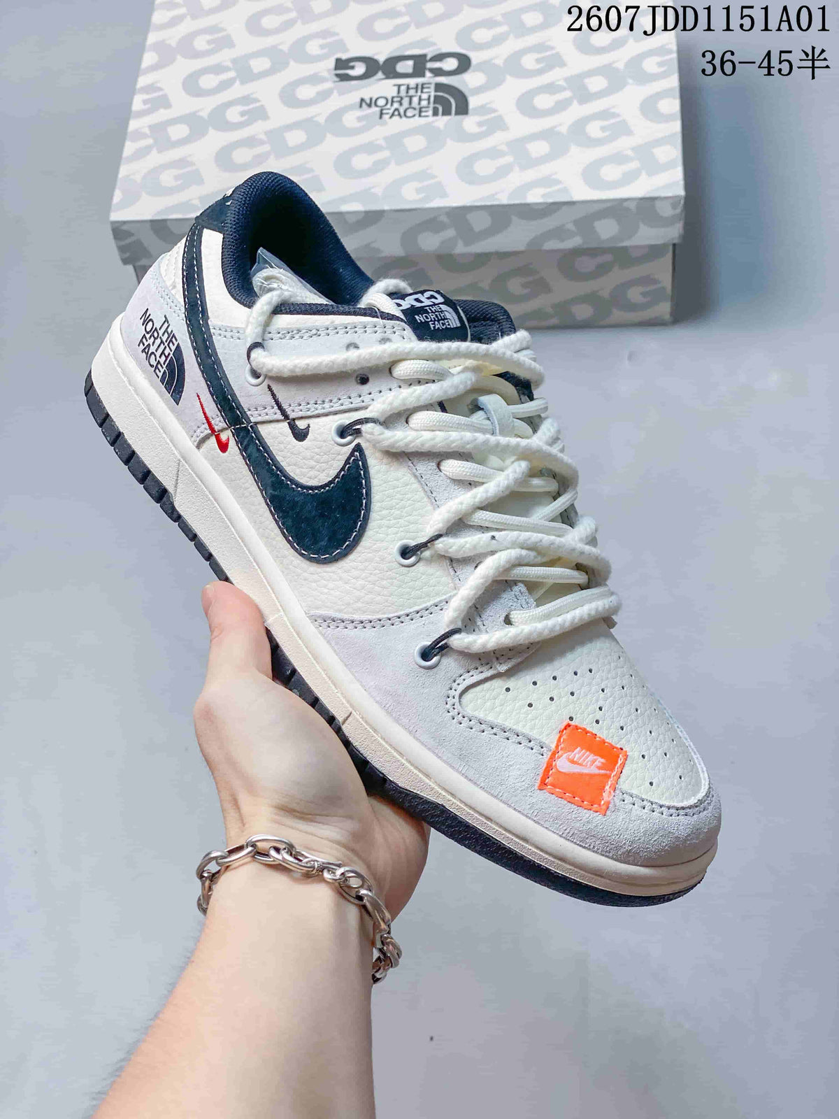 White low-top sneaker with dark swoosh, orange toe detail, and contrast branding.