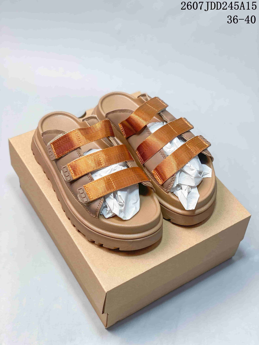 Pair of tan UGG GoldenGlow platform sandals with three metallic-gold straps, shown on a box.