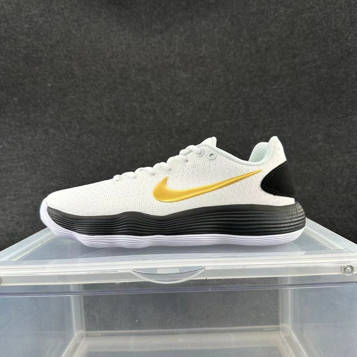 Side view of a white low-top Nike sneaker with a gold-tone swoosh, black heel panel, and black-and-white sole.
