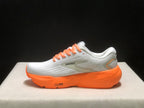 Side profile showing the Brooks side mark, white upper, orange midsole, and heel detailing.