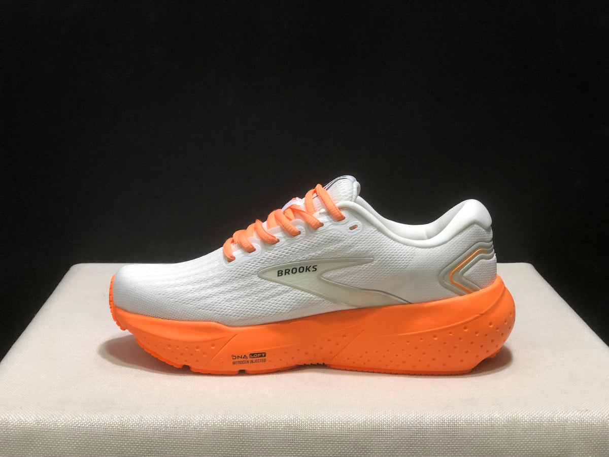 Side profile showing the Brooks side mark, white upper, orange midsole, and heel detailing.