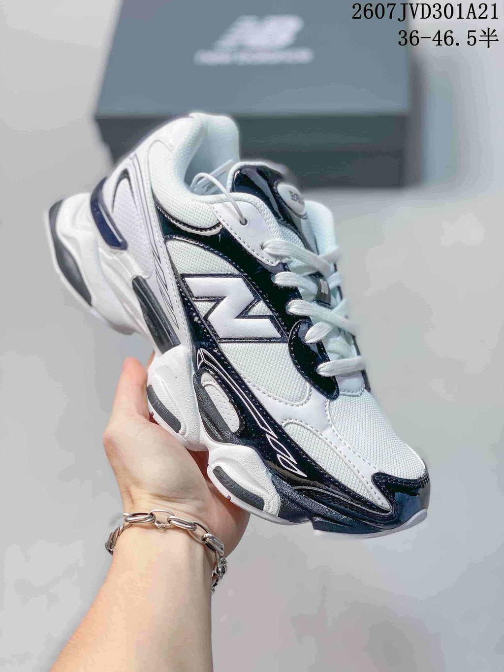 Angled side view of a white, navy, and black New Balance 9060R sneaker held in hand.