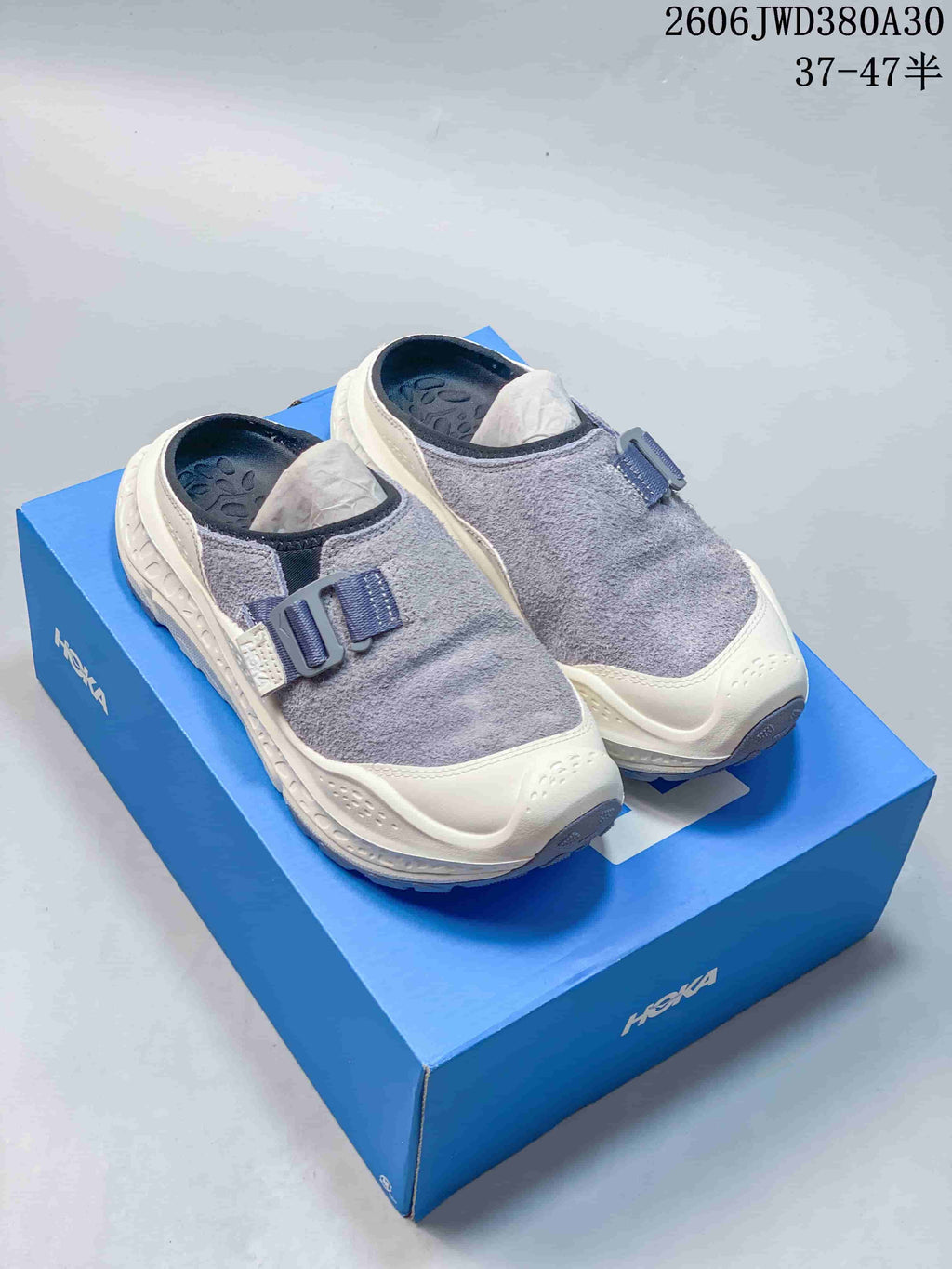 Pair of gray and cream HOKA Ora Primo EXT mule-style shoes on a blue box