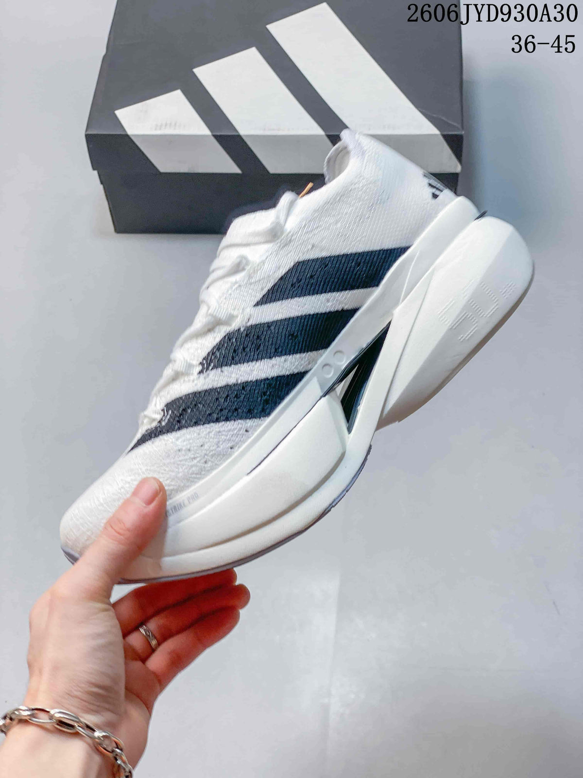 Side profile of a white adidas Adizero Prime X3 shoe with dark stripes and a sculpted sole.