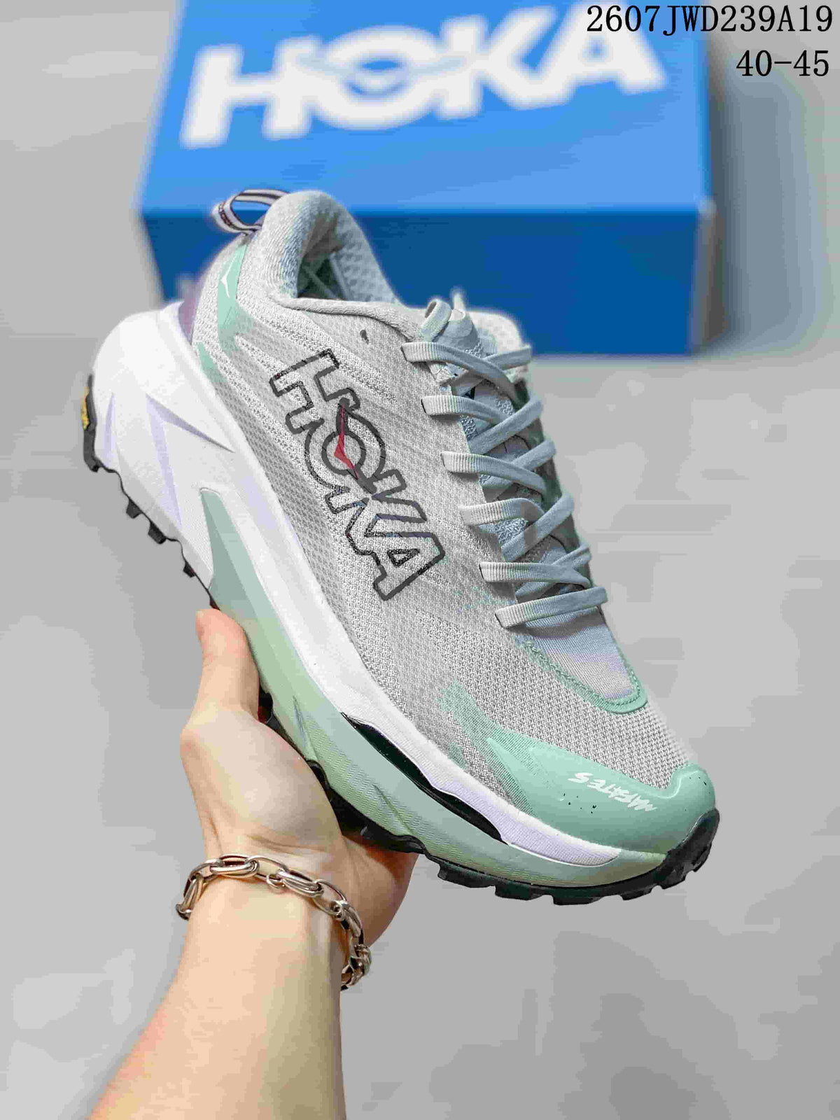 Angled side view of the HOKA running shoe showing the logo, gray upper, mint overlays, and layered sole.
