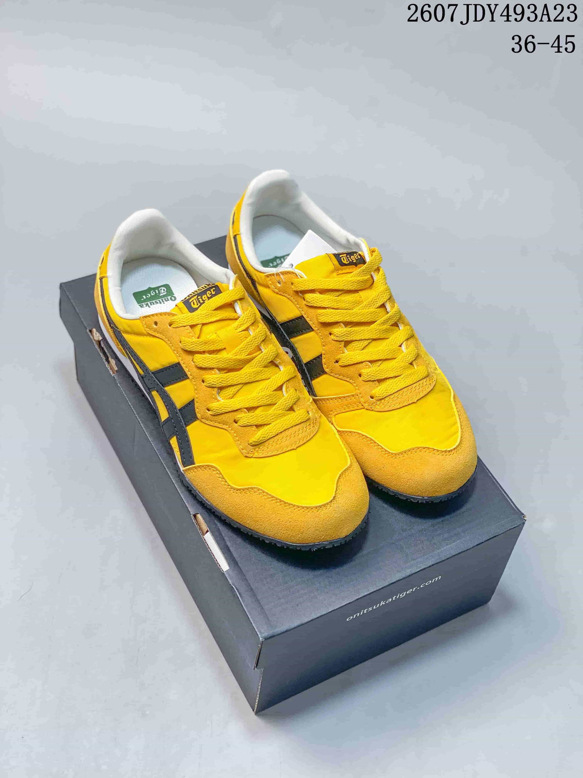 Yellow Onitsuka Tiger Serrano sneakers with dark contrast stripes displayed on a shoe box.
