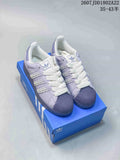 Pair of lavender and white Adidas Superstar sneakers displayed on a blue Adidas shoebox.