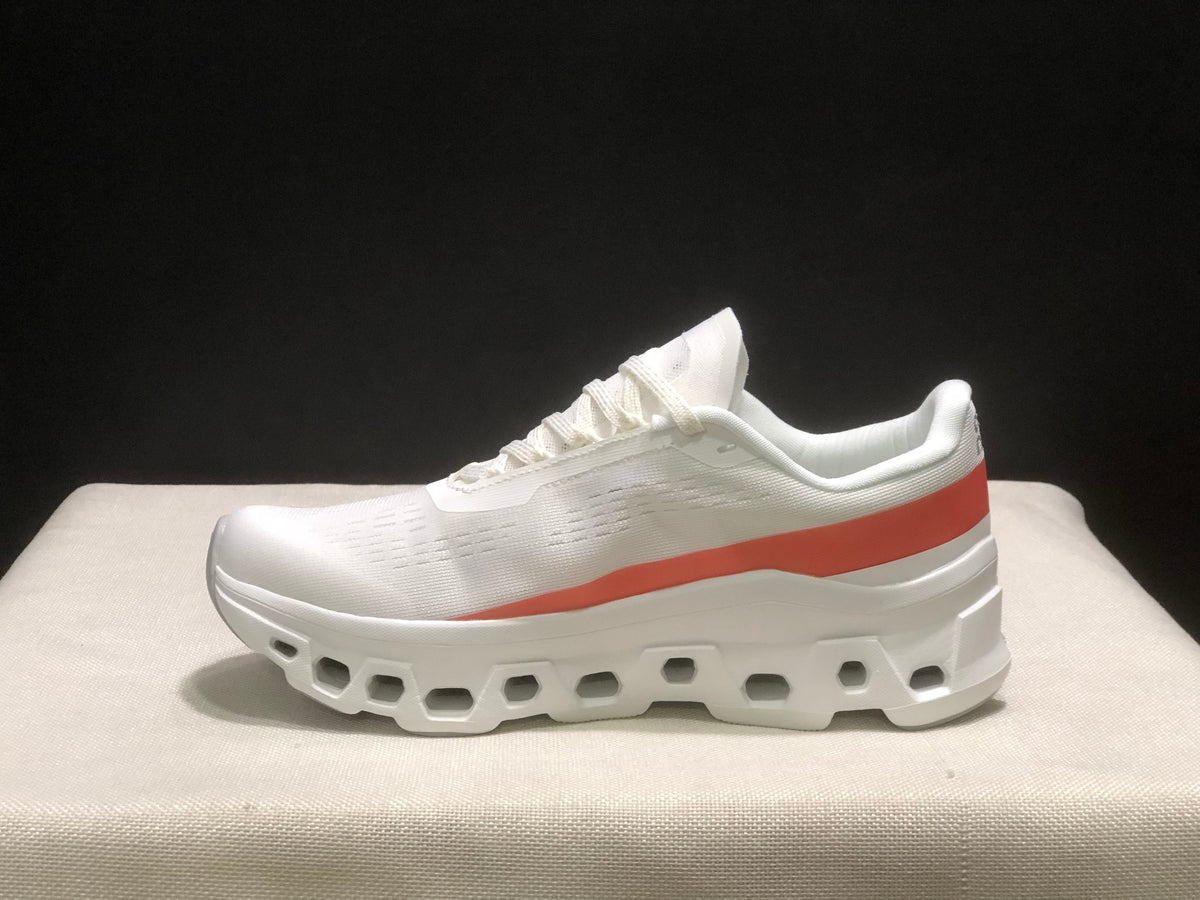 Side profile of one white sneaker with a coral-red stripe and structured outsole.