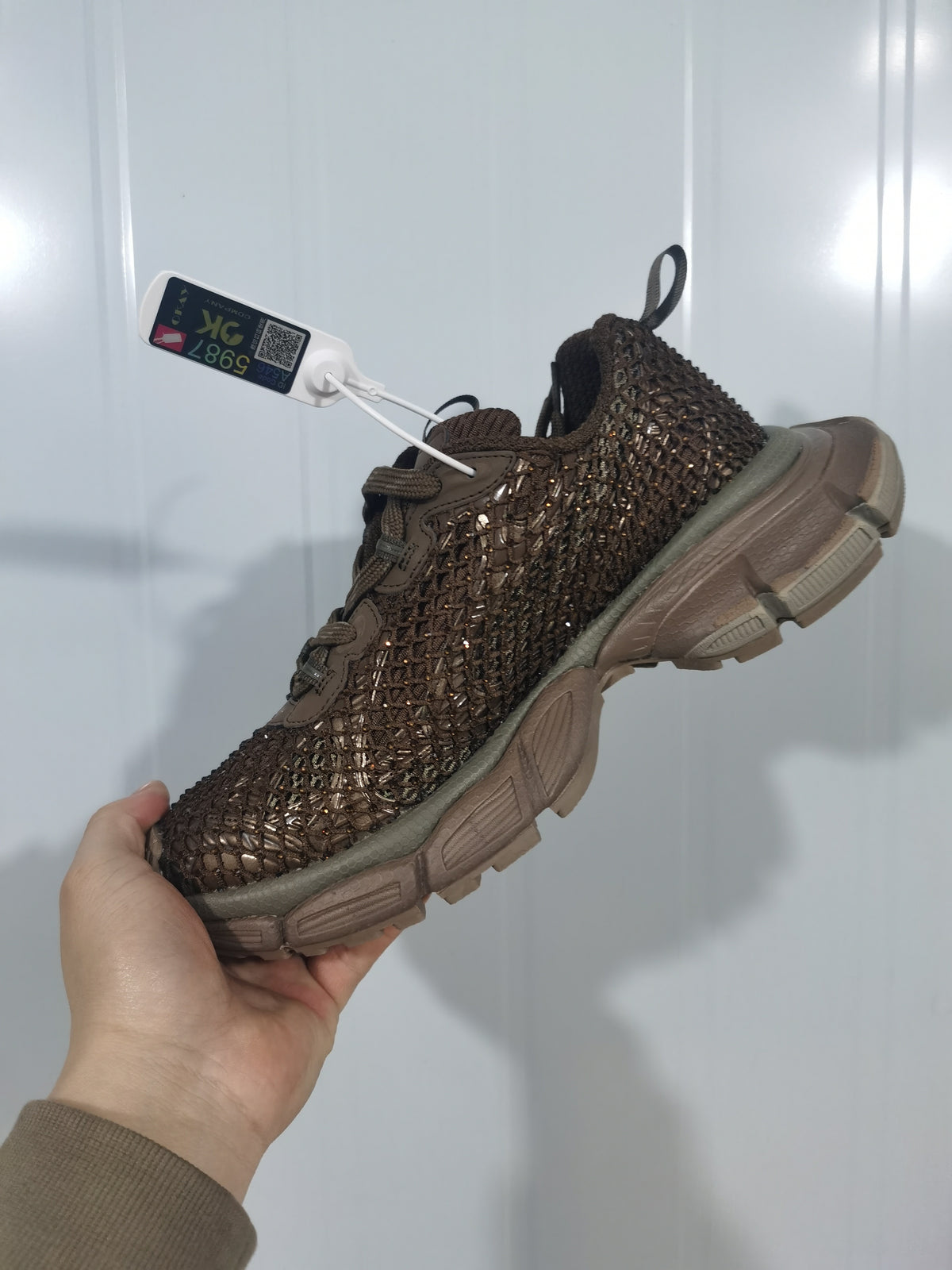 Angled view of a brown chunky sneaker with a textured fishnet-style upper, reflective detailing, tonal laces, and a sculpted outsole.