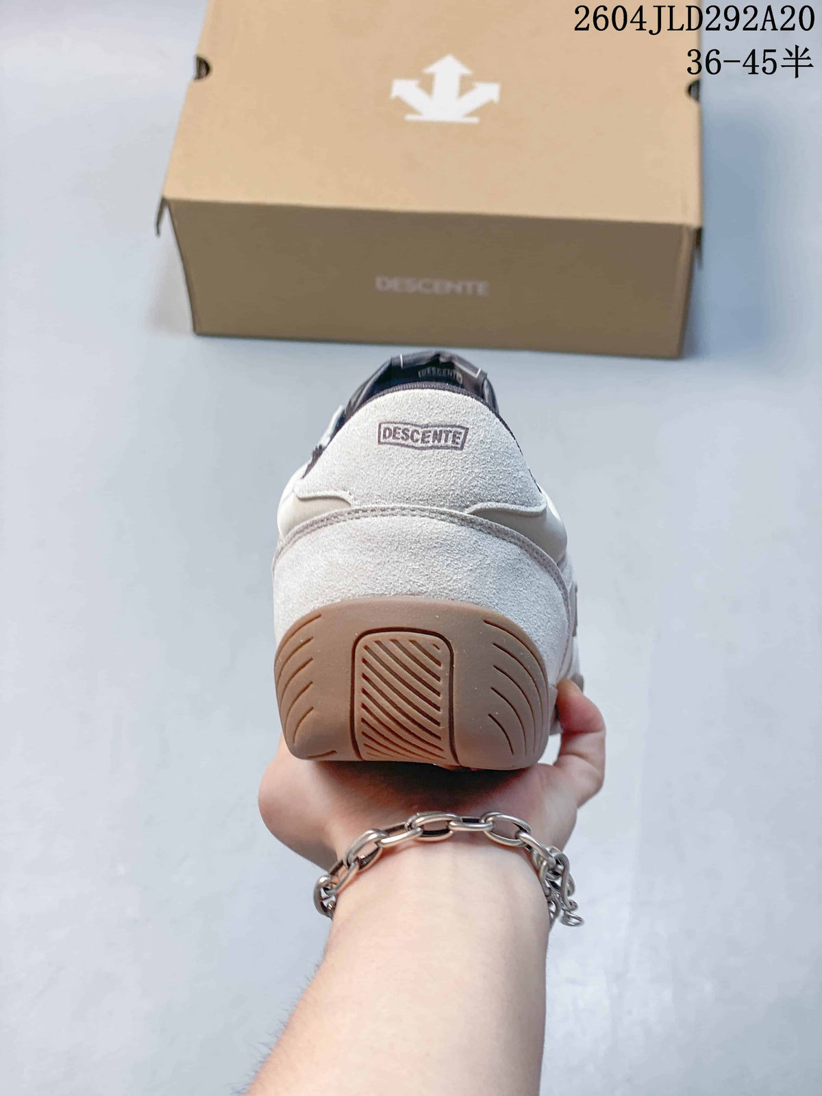 Rear view of a cream Descente sneaker showing the heel panel and gum-colored sole.