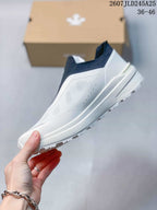 Side view of the white slip-on sneaker showing its textured upper, raised side panel, and layered white sole.