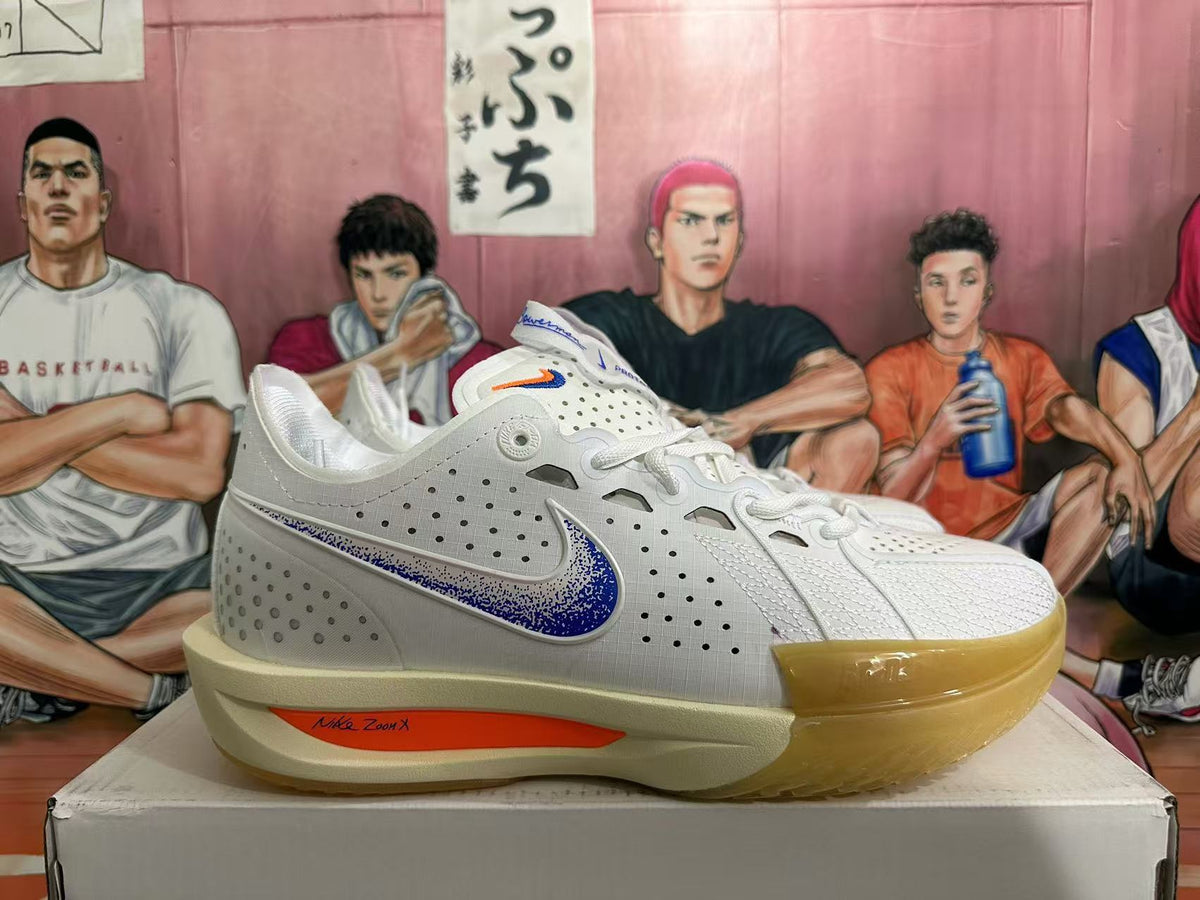 Side view of a white Nike basketball sneaker with blue speckled branding, an orange midsole accent, and a gum-colored outsole.