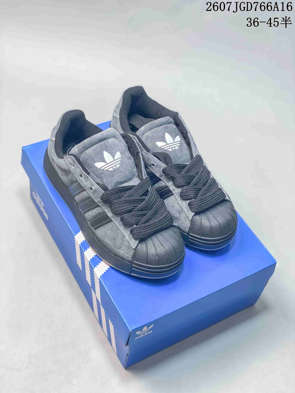 Pair of grey and black Adidas Superstar-style sneakers displayed on a blue shoe box.