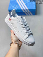 Side view of a white adidas Stan Smith sneaker showing perforated panels, a multicolor trefoil-style heel mark, and a navy heel accent.