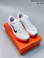 Pair of white Nike Vomero Plus shoes with dark Swooshes and orange and pink midsole accents, on an orange shoebox.