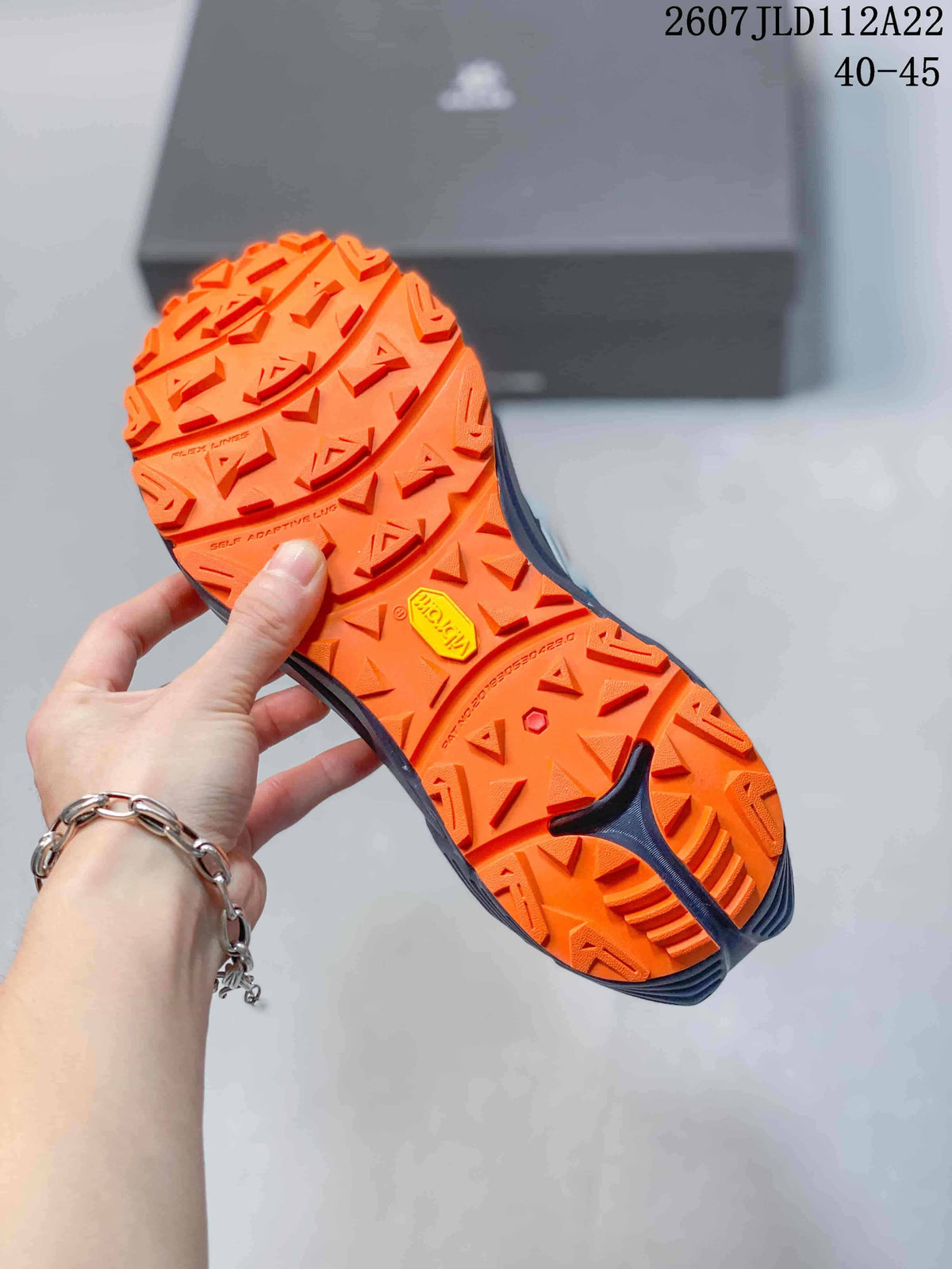 Orange lugged outsole of the Kailas C4 sneaker shown from below, with a visible Vibram mark and trail-style tread pattern.