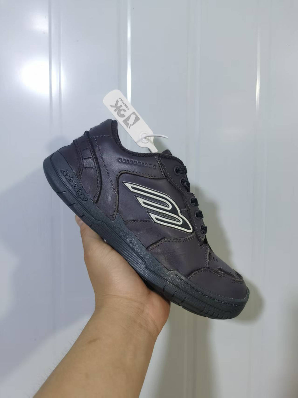 Three-quarter view of the grey sneaker showing the heel panel, side logo, laces and grooved outsole.