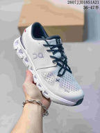 Front three-quarter view of the white and navy sneaker showing the perforated upper, side branding, laces, and cushioned sole.
