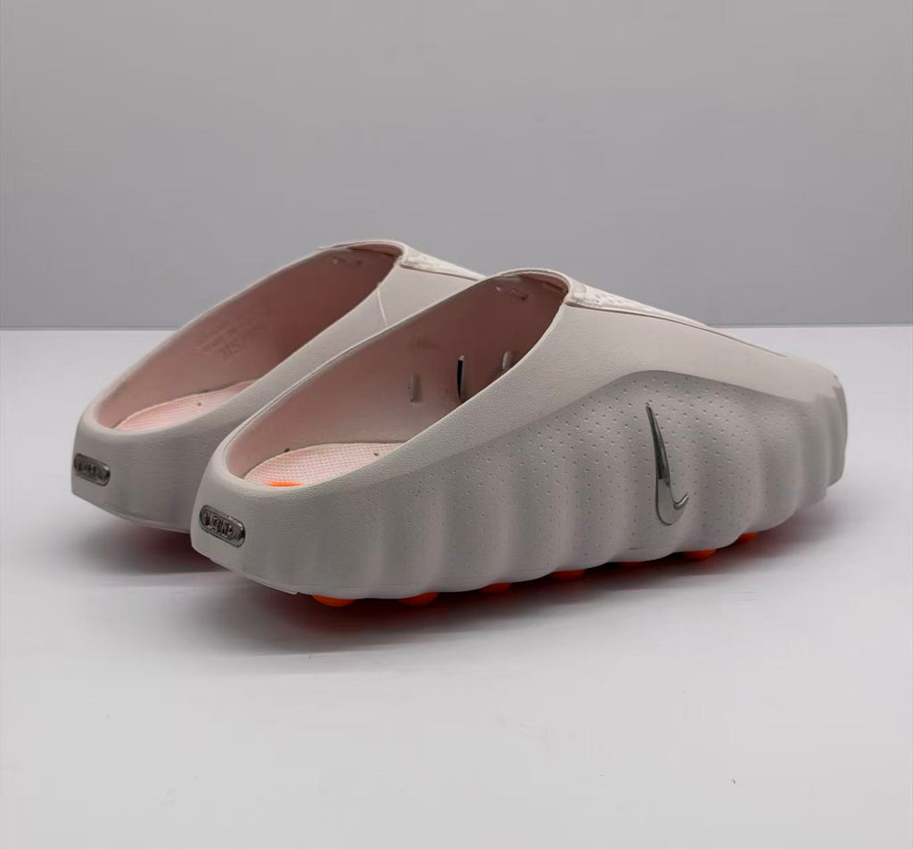 Rear three-quarter view showing the open-back design, side Nike branding, pink footbeds, and orange outsole details.