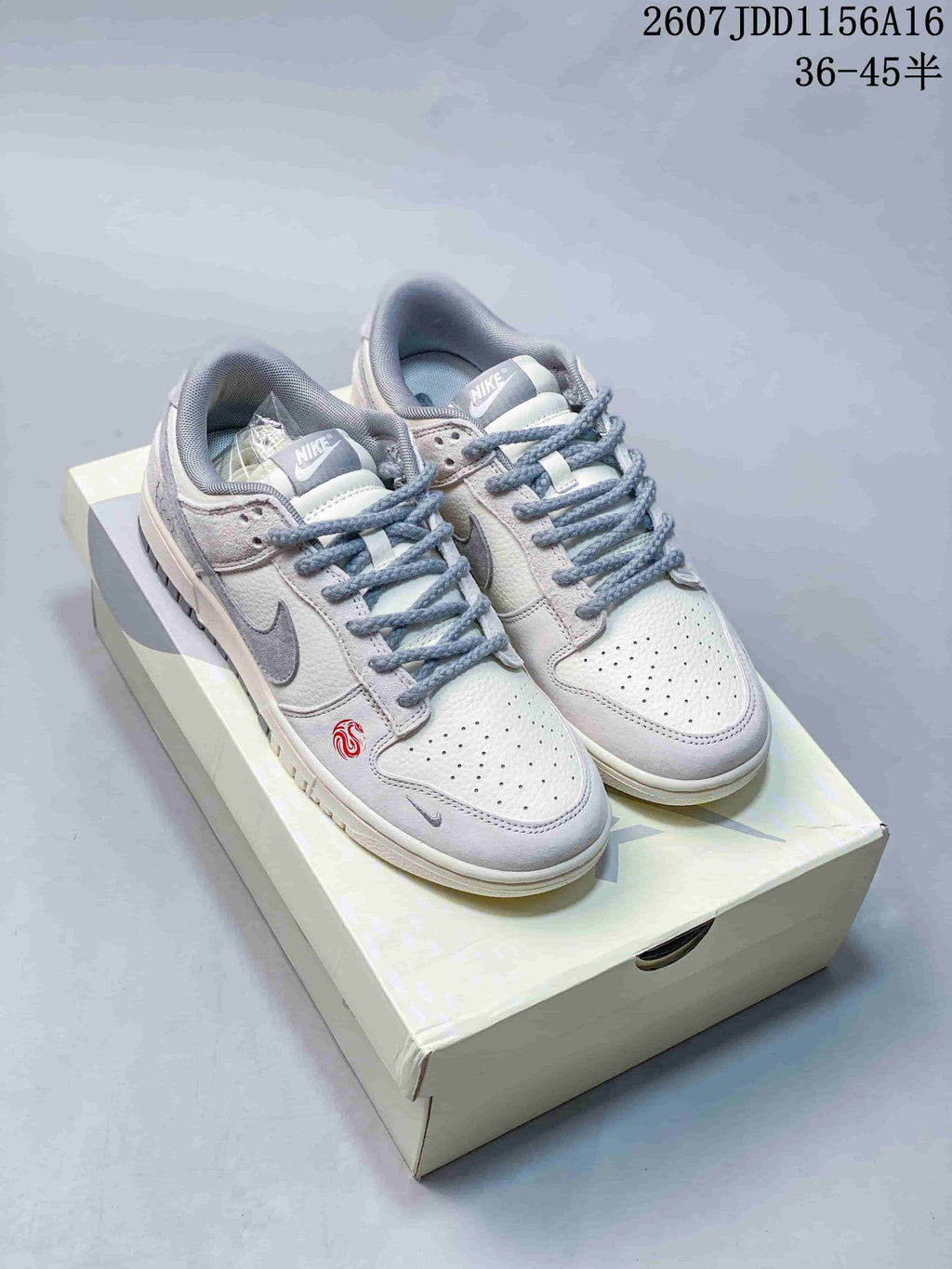 Pair of off-white and grey Nike SB Dunk Low sneakers displayed on a light-colored shoe box.