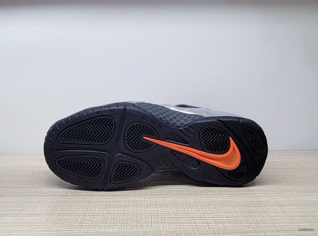 Outsole view of a black sneaker with an orange Swoosh detail