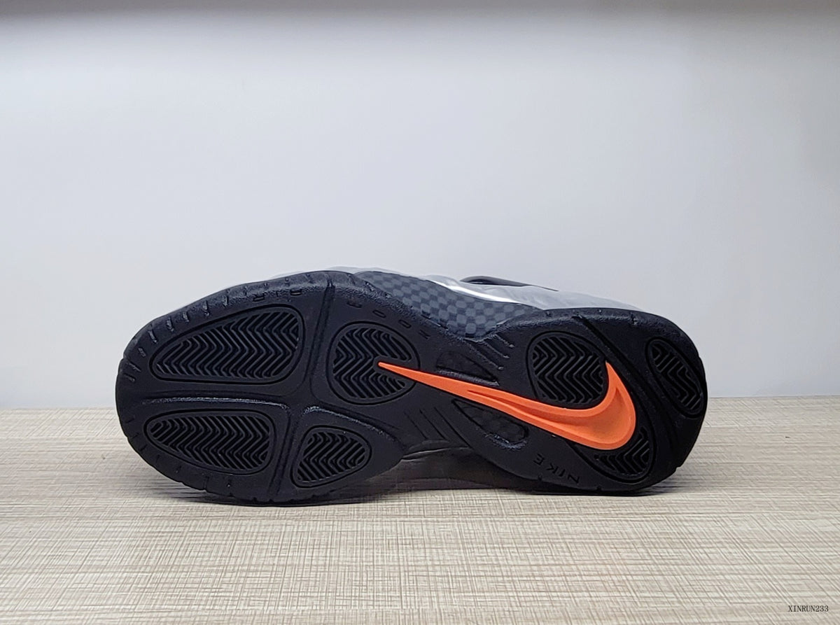 Outsole view of a black sneaker with an orange Swoosh detail