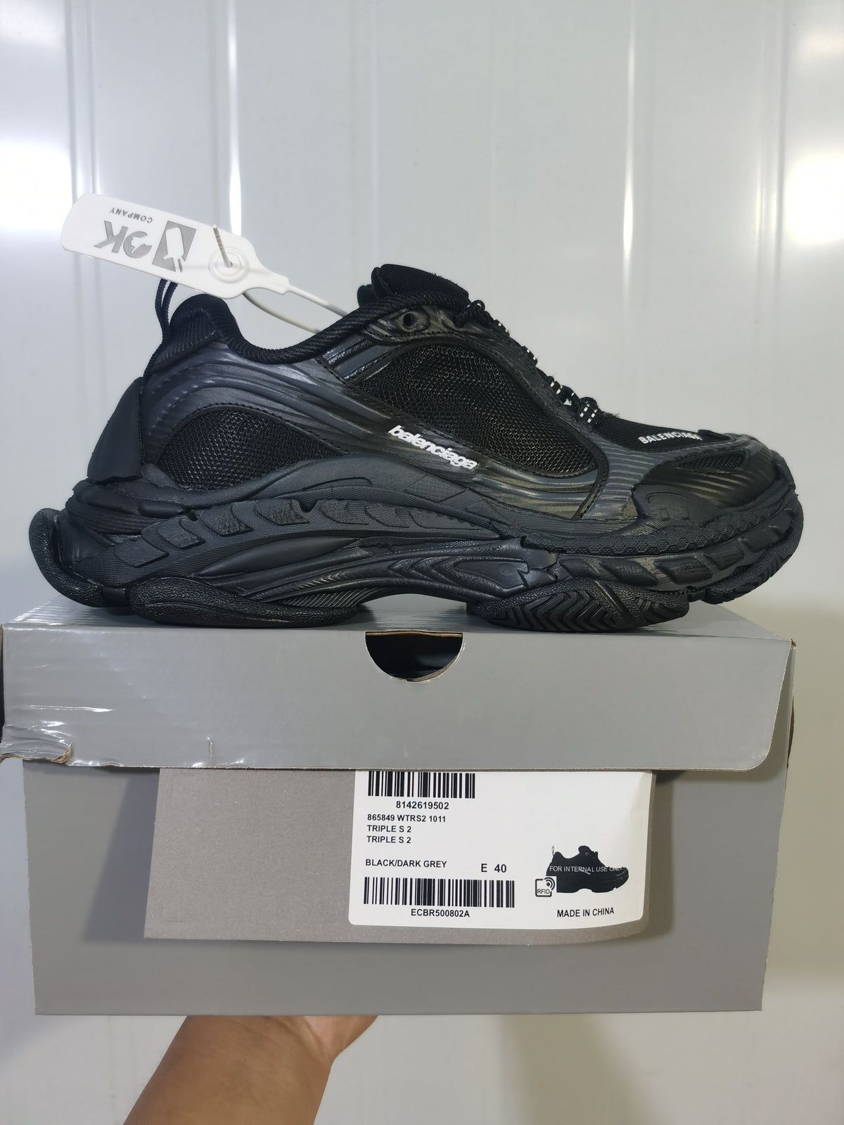 Side profile of the black and dark grey sneaker placed on its box, with the box label showing Triple S 2, style code 865849 WTRS2 1011 and sample size E 40.