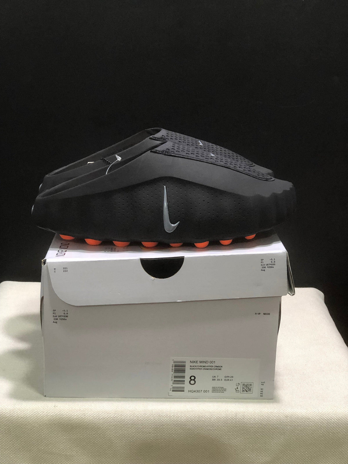Side view of black Nike Mind 001 slides with textured uppers, orange outsole pods, and a retail box.