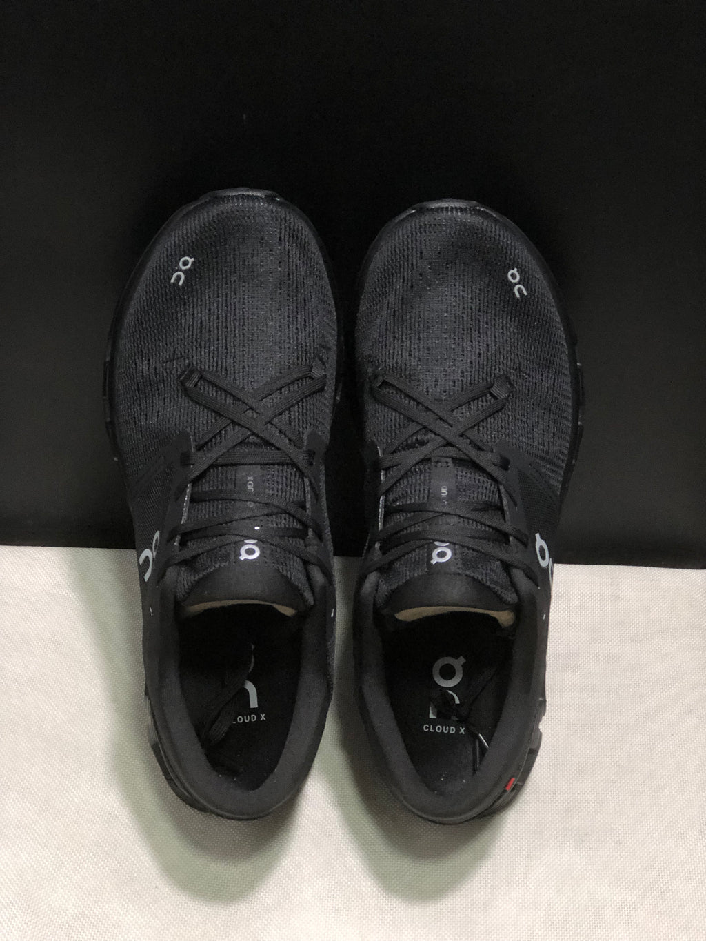 Top view of the black On Cloud X4 pair showing the lace-up construction and textured uppers.