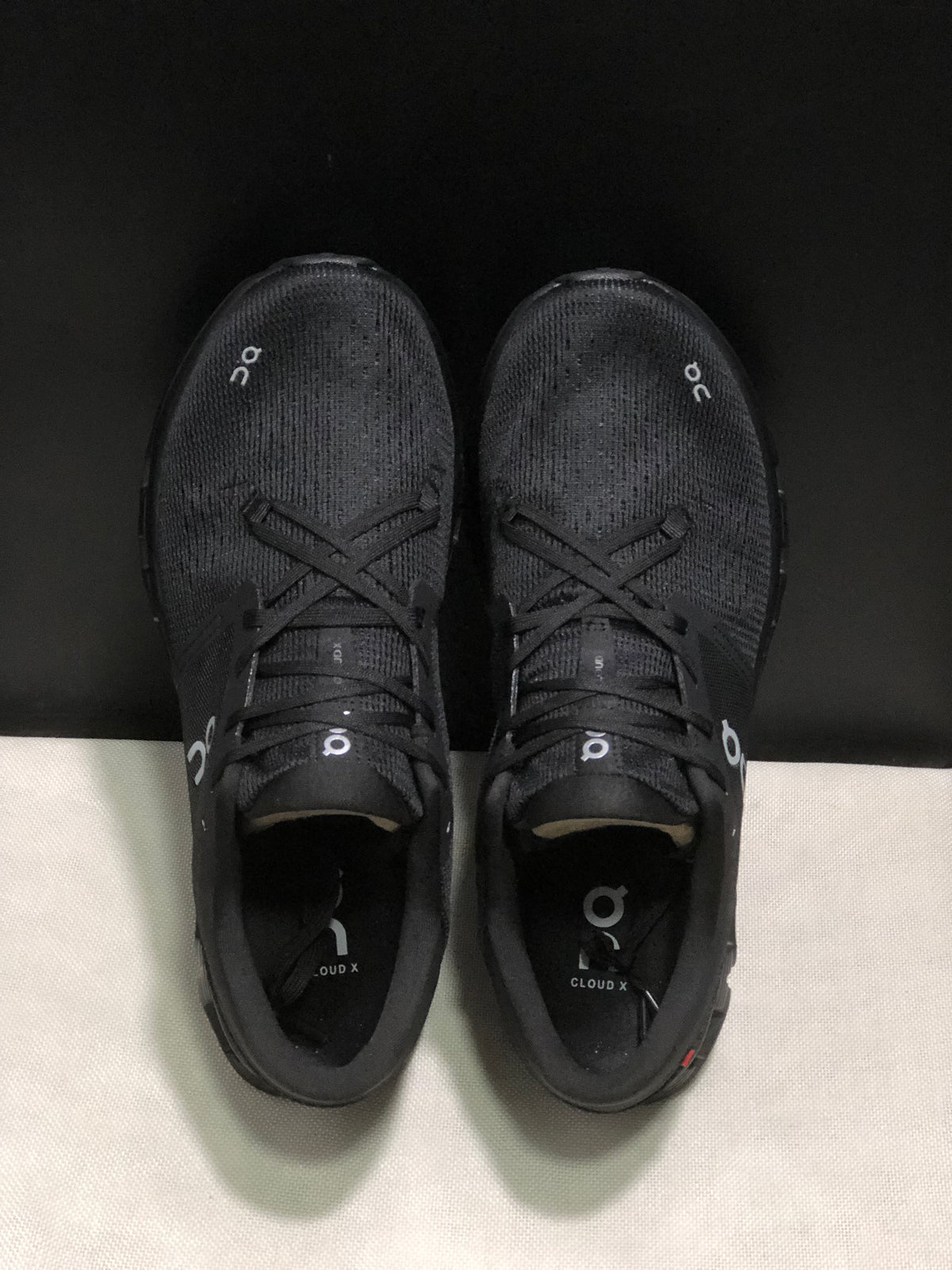 Top view of the black On Cloud X4 pair showing the lace-up construction and textured uppers.