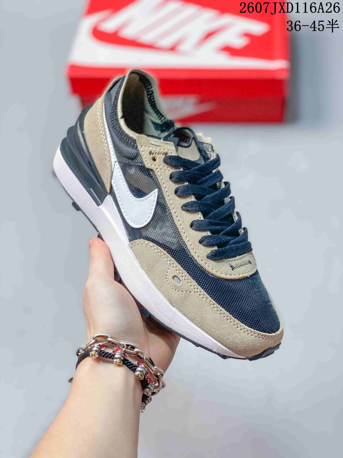 Angled side view of the Nike Waffle One GS sneaker showing the white Swoosh, brown overlays, dark upper panels, and textured outsole.