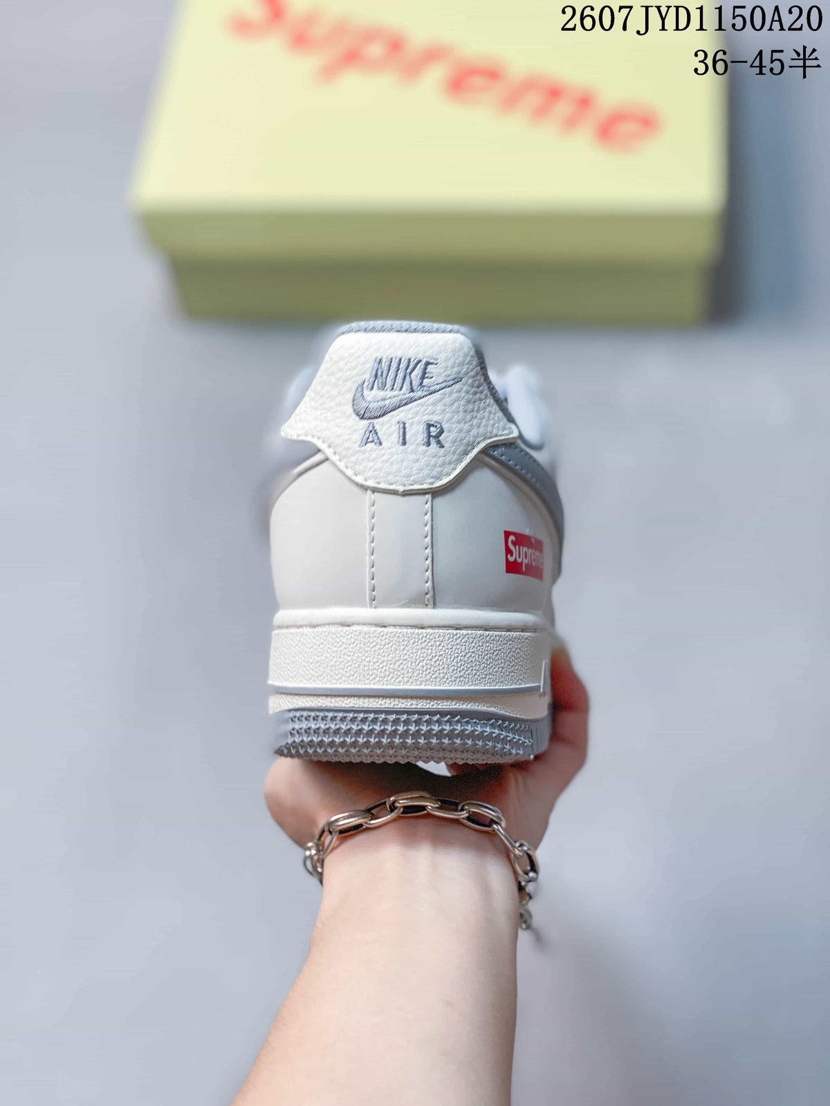 Rear view of a white sneaker showing the Nike Air logo on the heel tab, a Supreme logo accent, and a grey outsole.