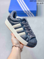 Close side view of a dark adidas shell-toe sneaker with light three-stripe detailing.