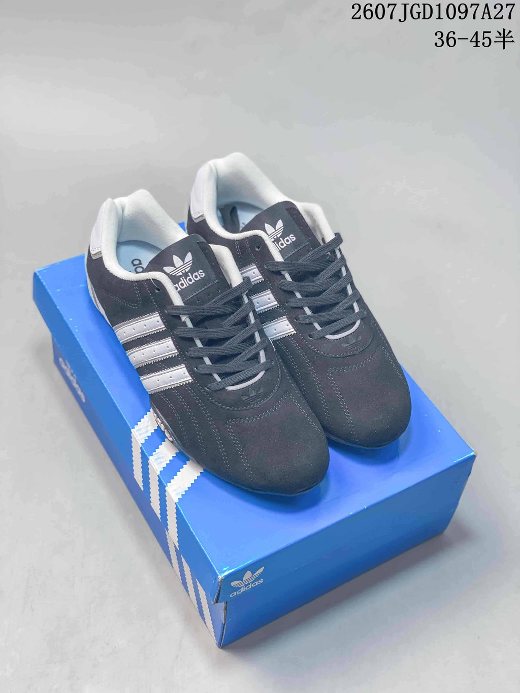 Pair of black and white Adidas low-top sneakers displayed on a blue shoebox.