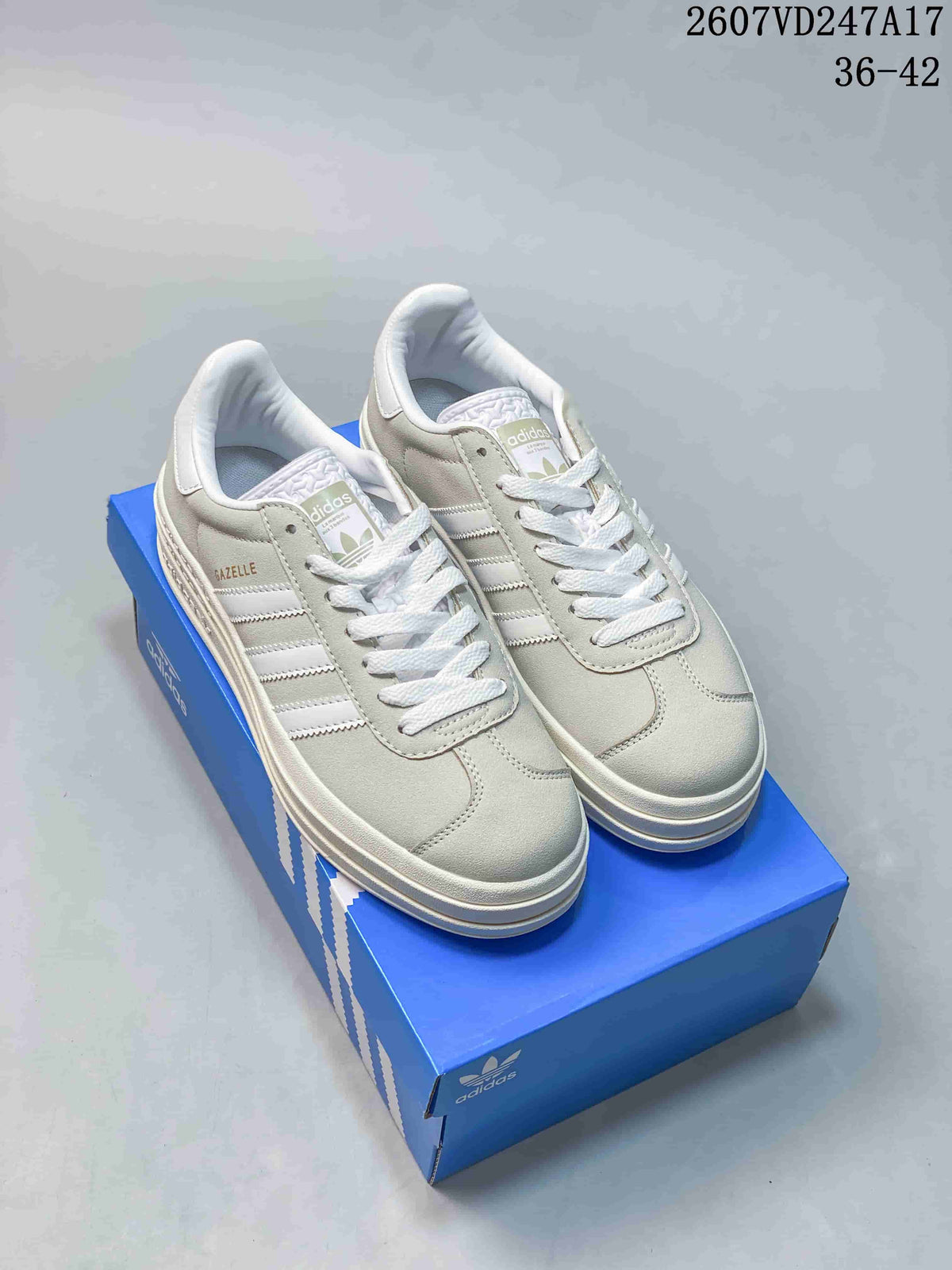 Pair of light gray adidas Gazelle Bold sneakers with white laces, side stripes, raised soles, and a blue adidas shoe box.