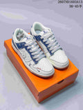 Pair of white and blue low-top sneakers shown on an orange shoebox, with blue patterned panels and monogram-style details.