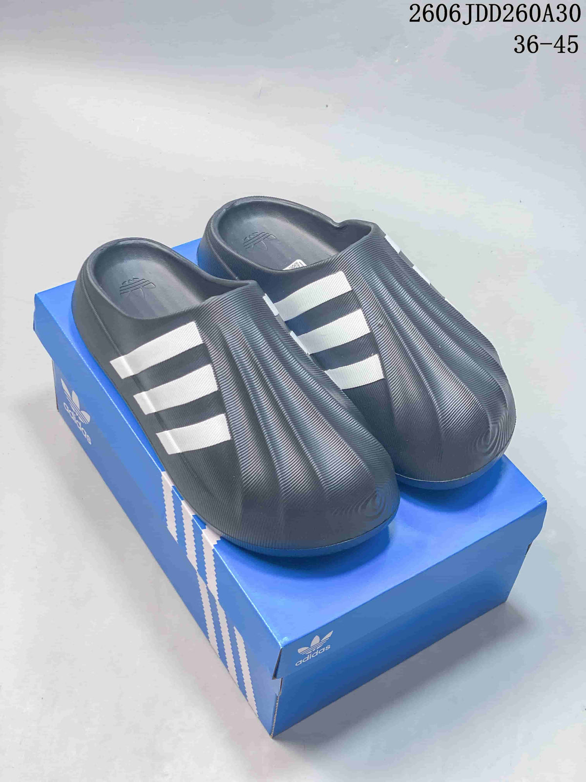 Pair of charcoal adiFOM Superstar mules with light-colored side stripes on a blue shoebox.