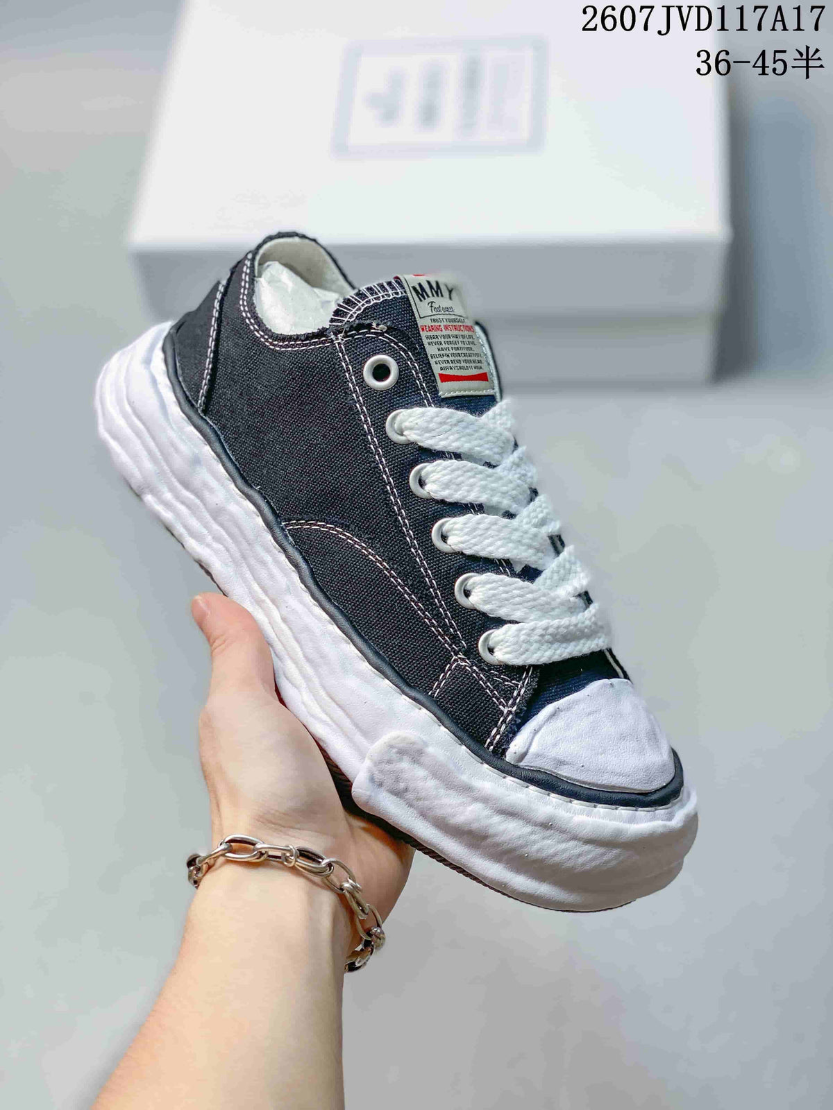 Close side view of a black MMY canvas sneaker showing contrast stitching, metal eyelets, tongue label and textured white sole.