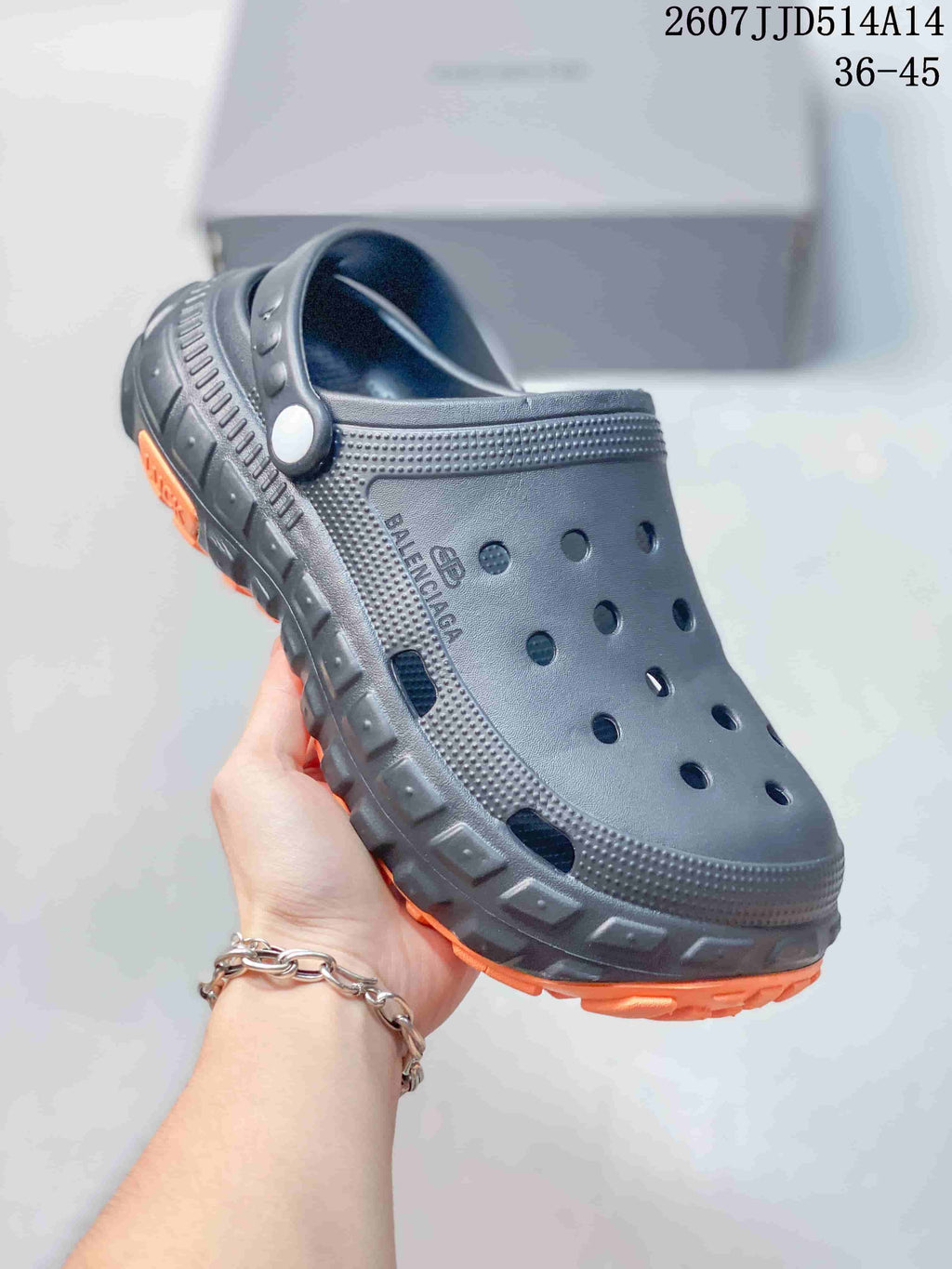 Close-up side view of a black perforated clog showing the strap, branding and textured chunky outsole.