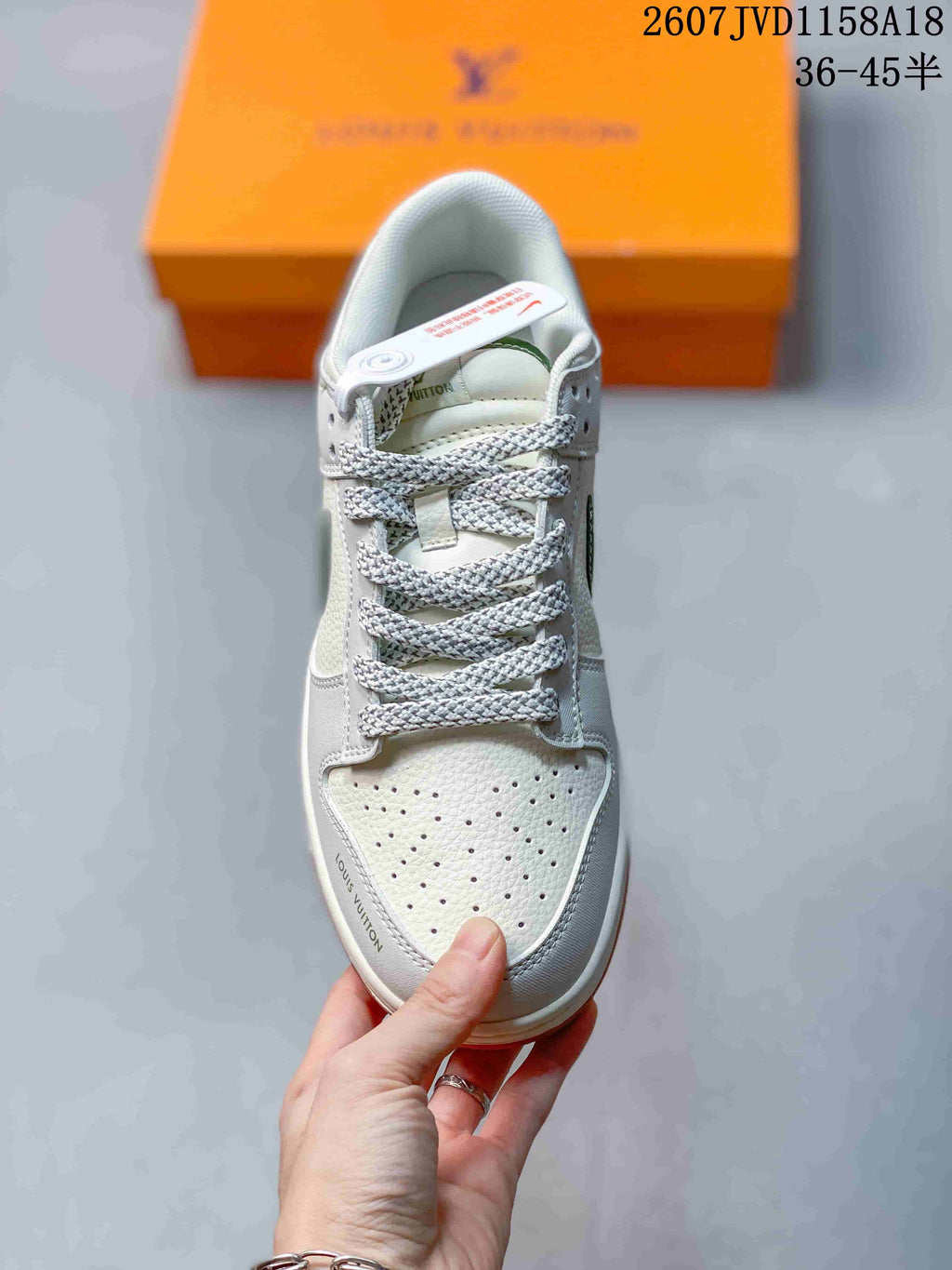 Top view of a white sneaker with perforated toe panel, braided laces, and branding details; an orange box is behind it.